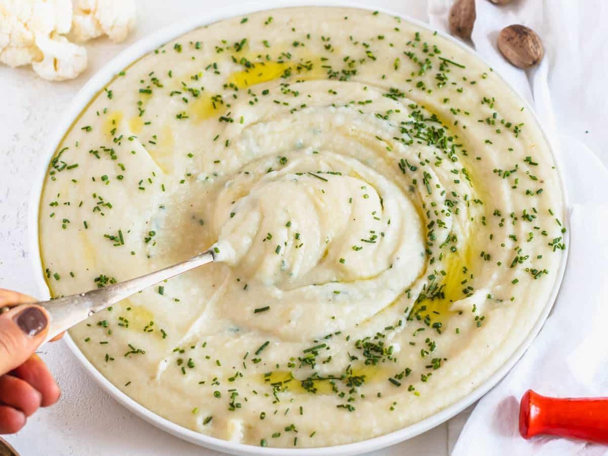 Blumenkohl-Kartoffelpüree mit Hand, die einen Löffel hält