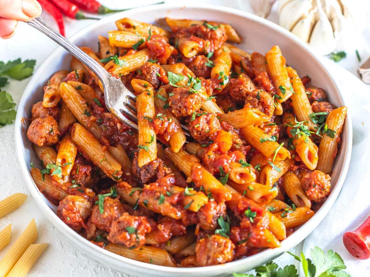 Penne Arrabbiata in einer weißen Schüssel mit einer silbernen Gabel, die die Pasta durchsticht