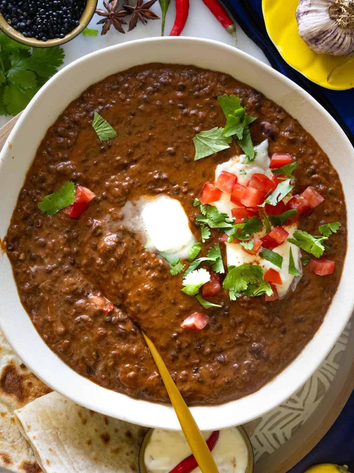 Schwarzes Linsen Dal serviert mit Raita, Koriander und einem Stück Butter.