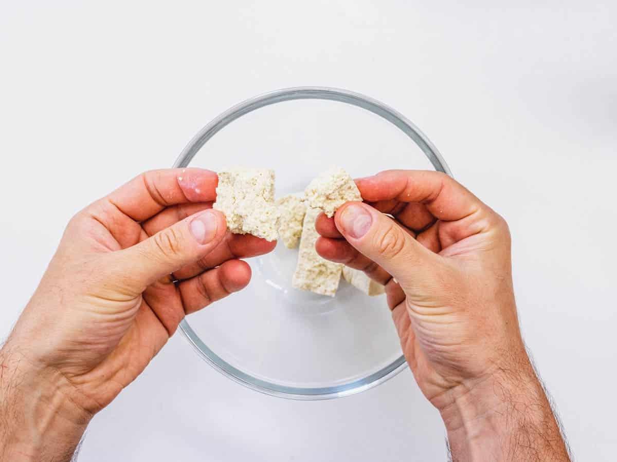 Tofu mit Händen auseinanderbrechen.