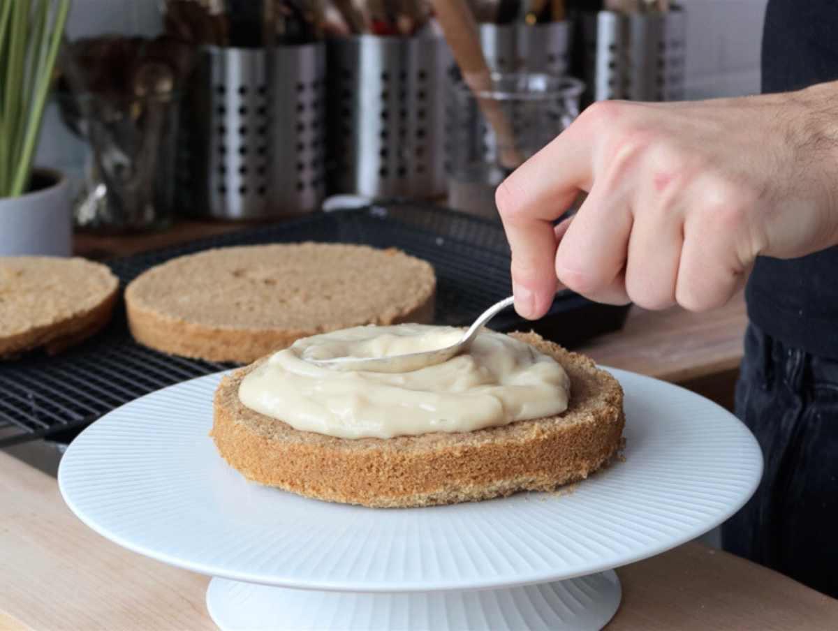 Veganer Kokoskuchen 6 Hand trägt veganen Pudding auf den veganen Kokoskuchen auf