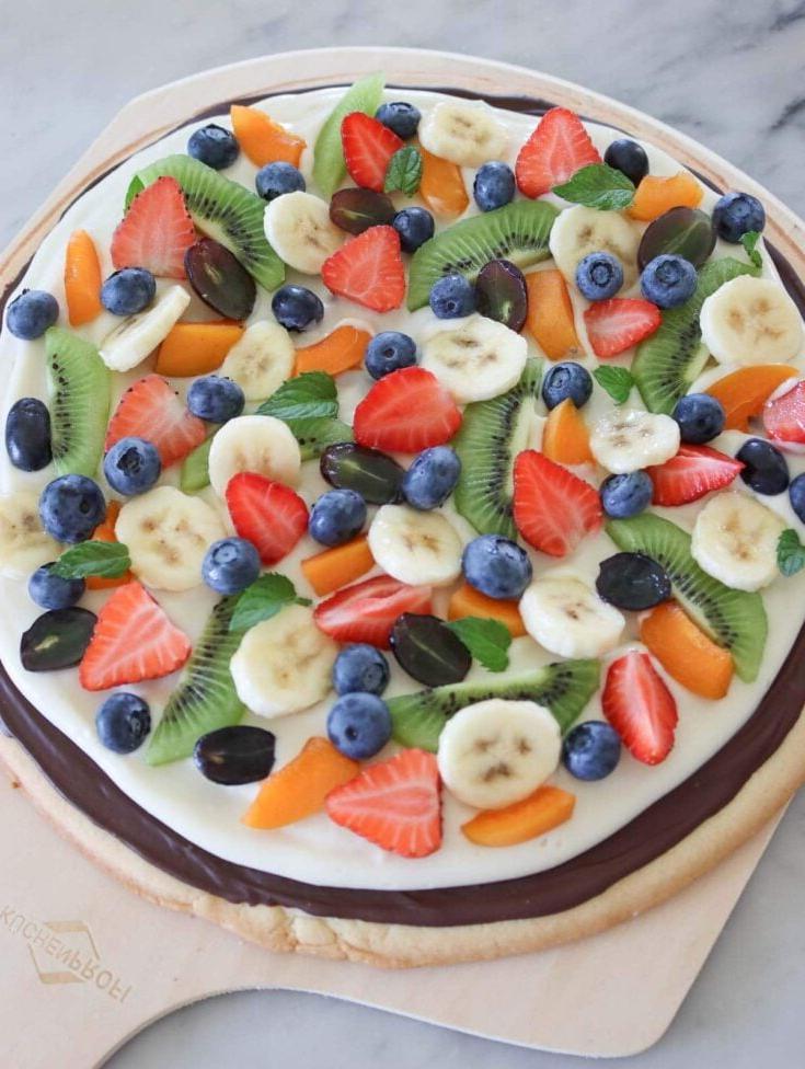 Bunte vegane Fruchtpizza mit verschiedenen Beeren und Sahne.