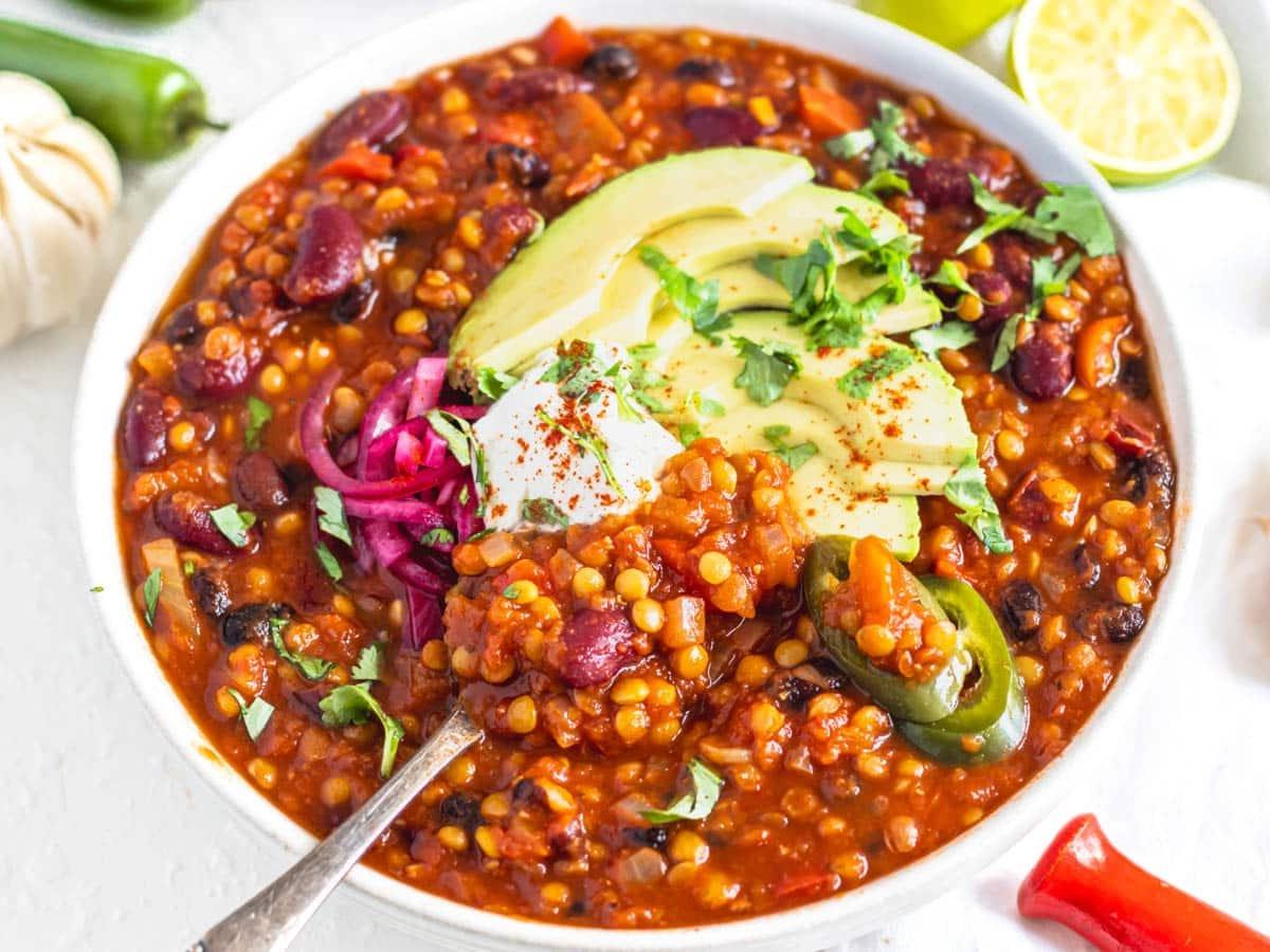 Linsen-Chili in einer Schüssel mit Sauerrahm, Avocado und eingelegten roten Zwiebeln