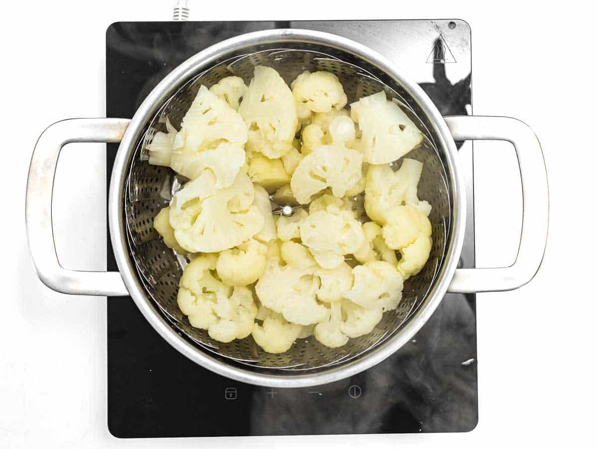 Gedämpfter Blumenkohl in einem Dampfkorb, bereit für die Zubereitung von Blumenkohl Alfredo.