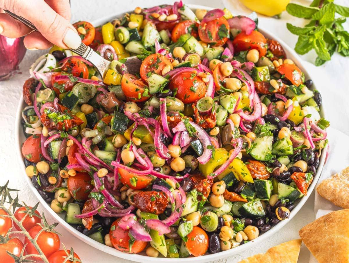 Mediterranean salad with sumac onions and hand holding a silver spoon