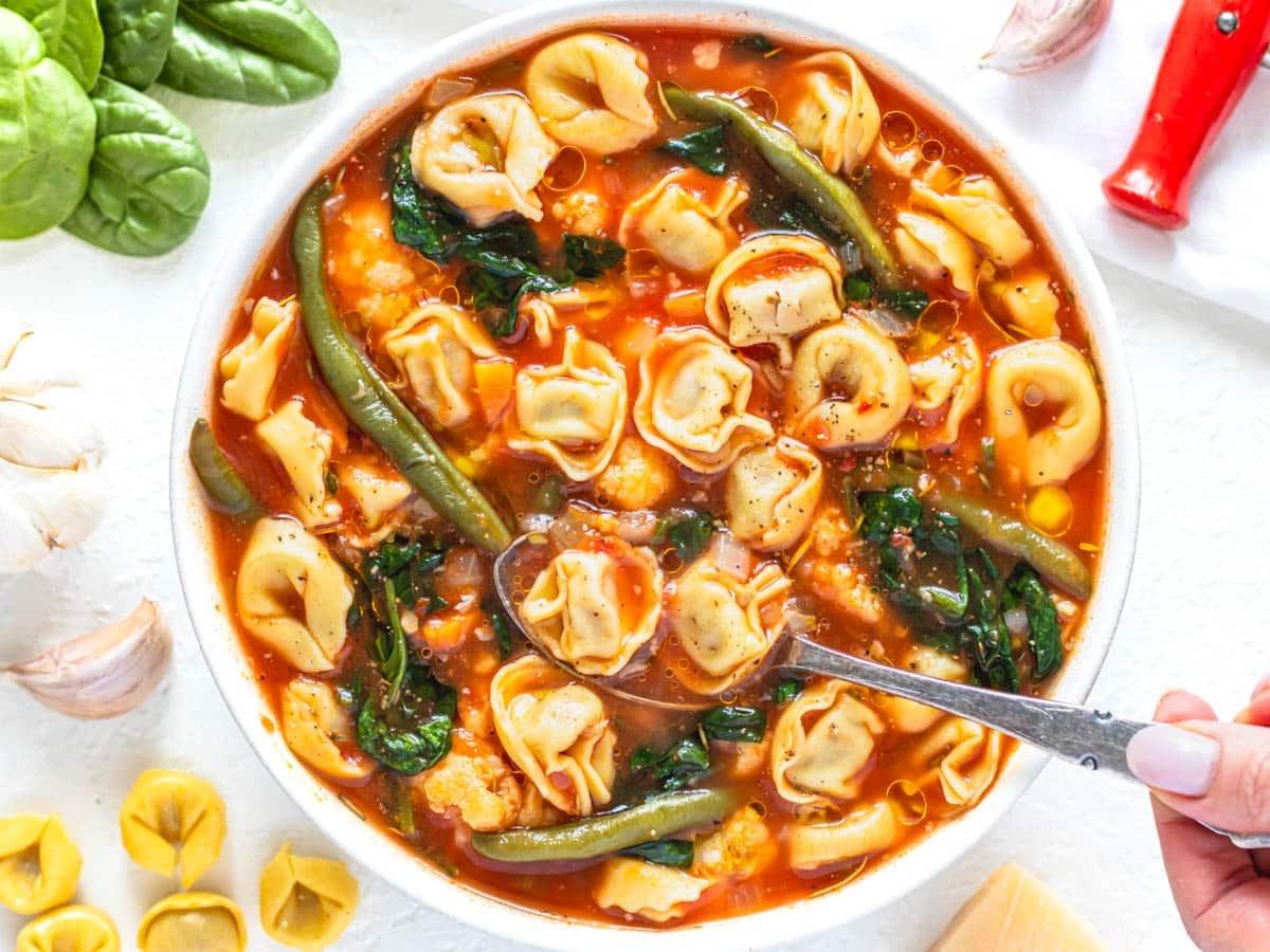 Tortellini-Suppe mit Spinat und einer Hand, die einen silbernen Löffel hält