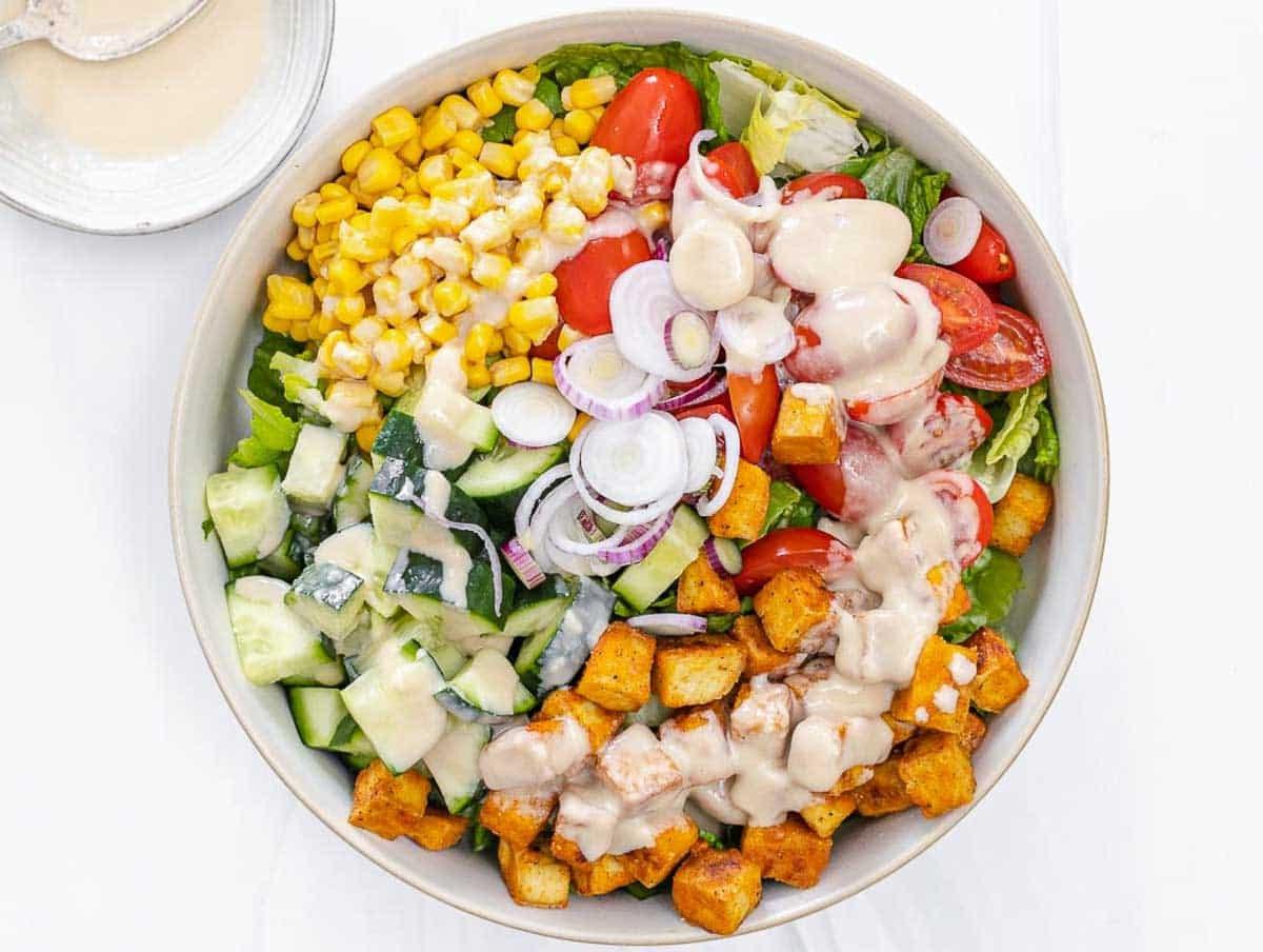 Tofusalat in einer Salatschüssel mit Tahini-Dressing darauf, vor dem Mischen.
