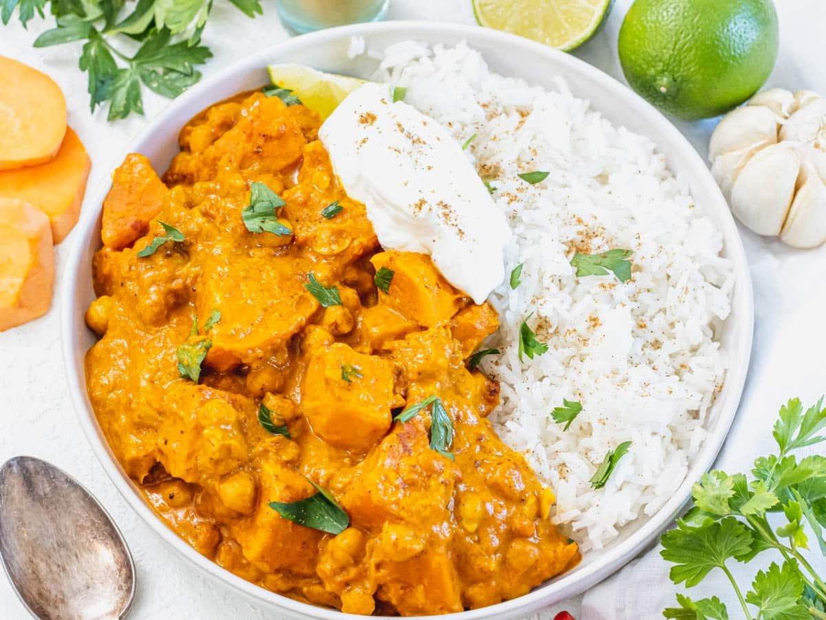 Süßkartoffel-Curry serviert mit Joghurt, Zitrone und frischem Koriander als Toppings.