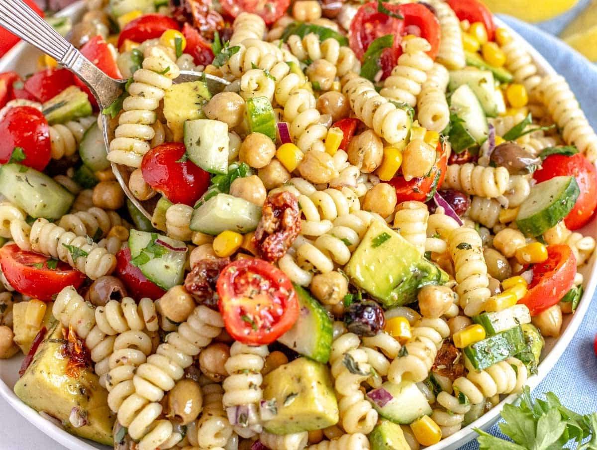 Kichererbsen-Nudelsalat mit einem silbernen Löffel und Avocado-Würfeln
