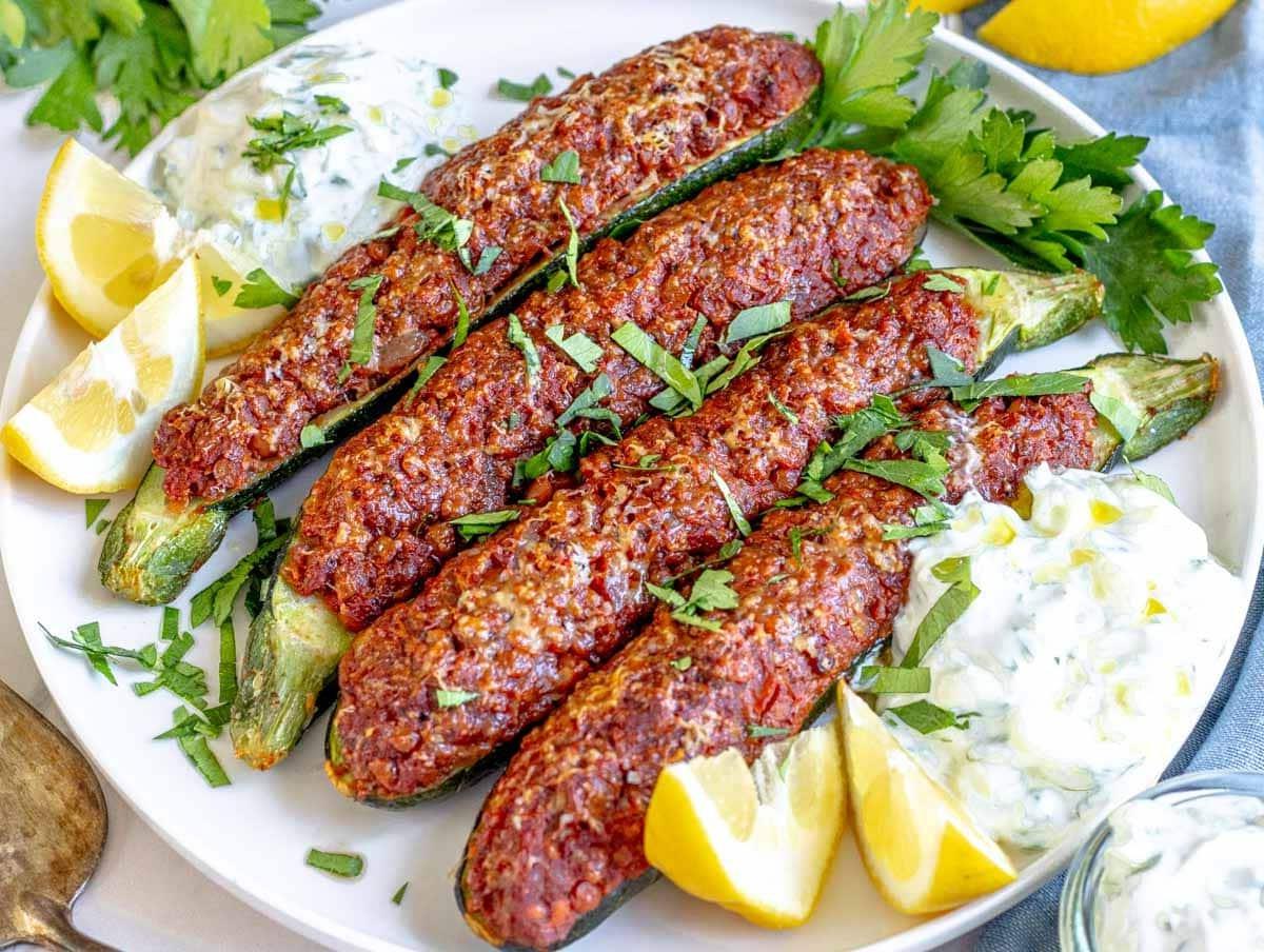 Zucchini-Boote 8 Zucchiniboote garniert mit frischer Petersilie und Zitronenspalten auf einer Holzplatte.