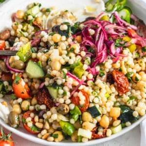 Mediterraner Couscous Salat mit Feta und frischem Gemüse, auf einem Teller angerichtet.