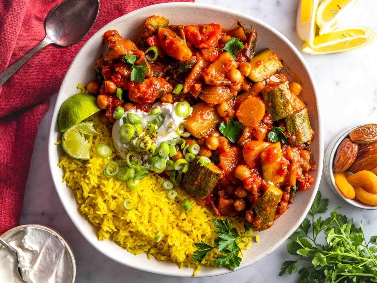 Tajine in einer Schale serviert mit Safranreis, Joghurt, Petersilie und Limettensaft.
