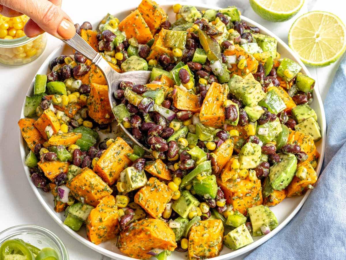 Salat aus schwarzen Bohnen mit einer Hand, die einen Löffel hält, und einer Limette im Hintergrund
