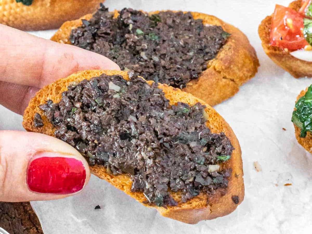 Oliven-Tapenade Crostini und Hand