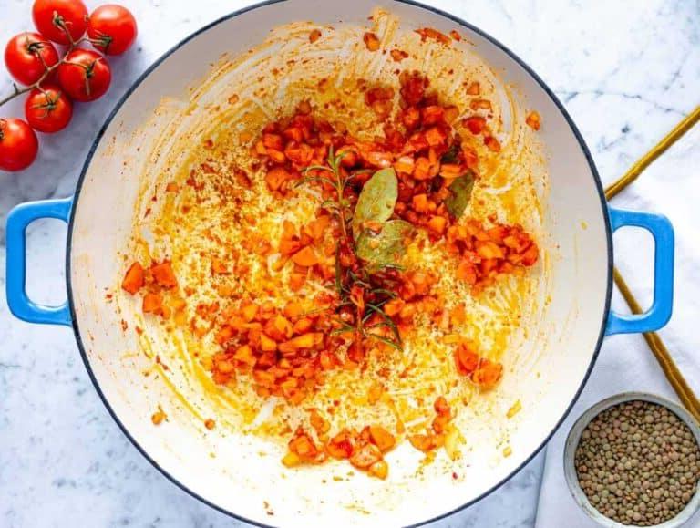 Geschmacksbasis mit Zwiebel, Karotte und Tomatenmark in einer Pfanne anbraten.