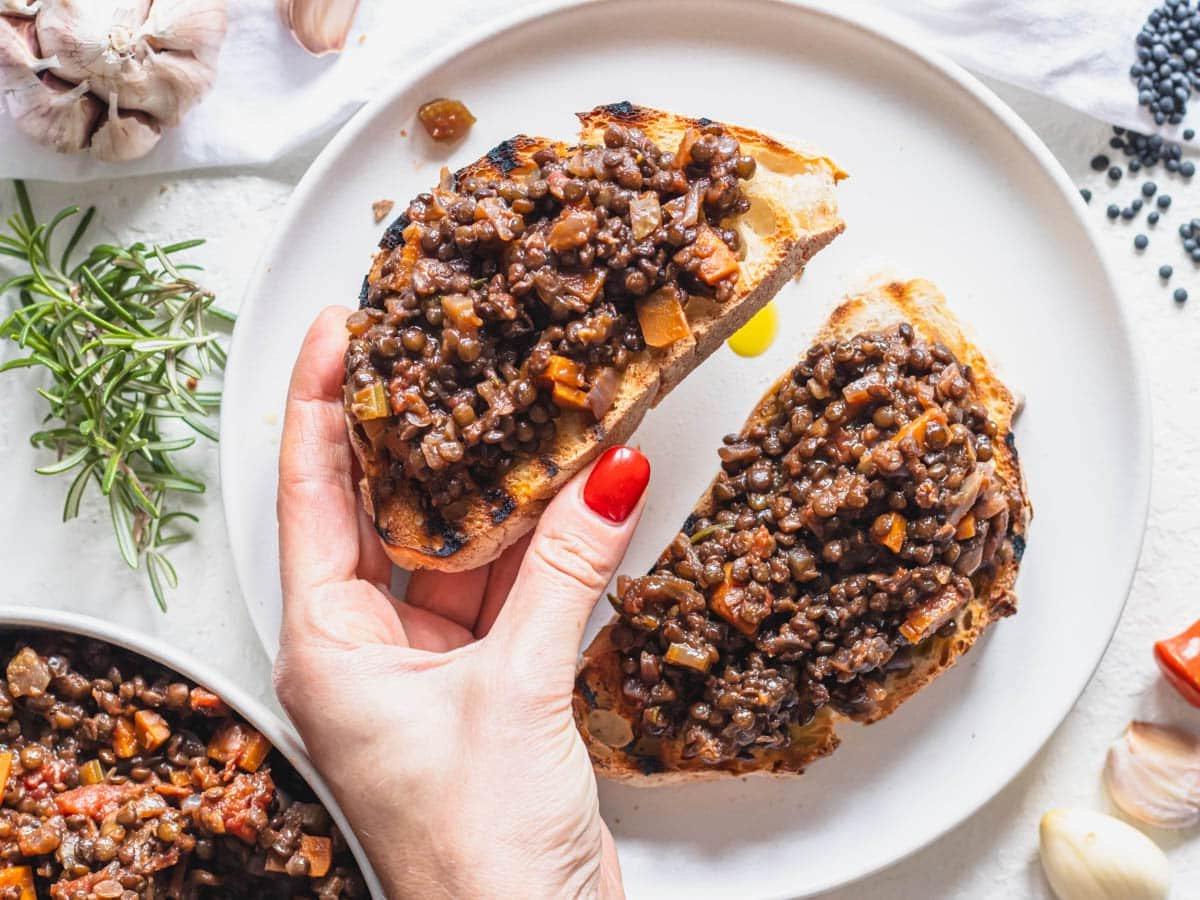 Schwarze Linsen auf Bruschetta mit Hand und rotem Nagel