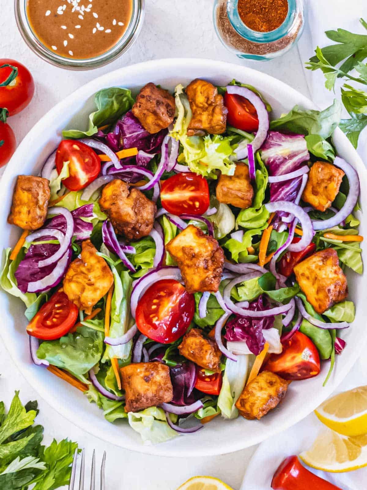 Tofu aus der Heißluftfritteuse auf einem Salat. Grüne Blätter, Kirschtomaten und goldene Tofuwürfel.