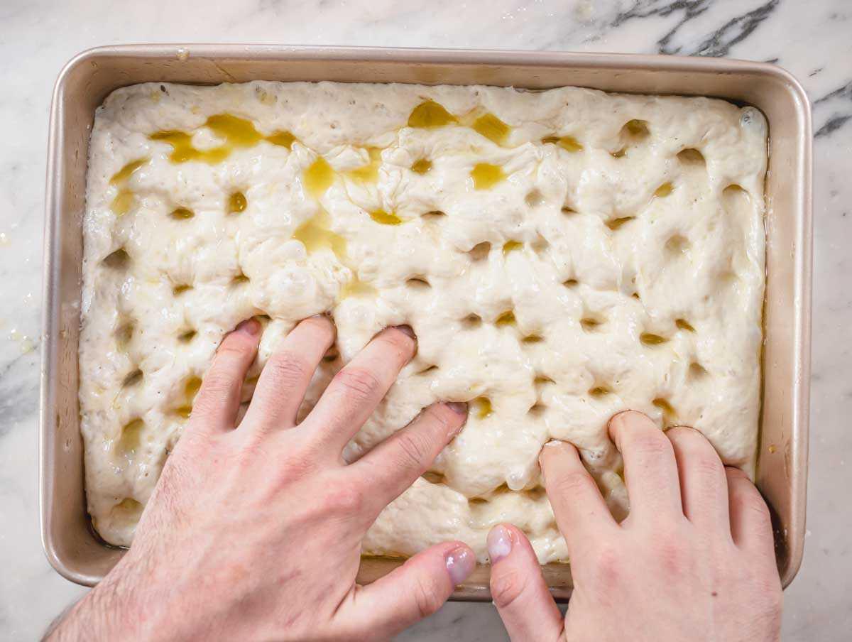 Nico formt Dimples im Focaccia-Teig und bereitet das Topping vor.