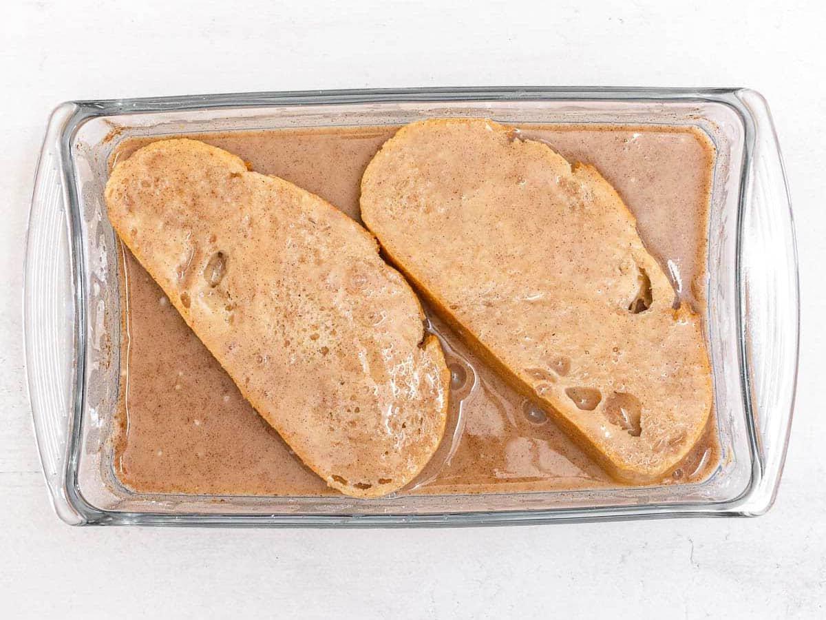 two slices of bread soaked in a cinnamon batter in a casserole