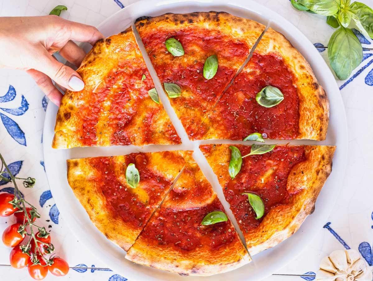 Hausgemachte Pizza mit Marinara-Sauce und einer Hand, die ein Stück Pizza nimmt